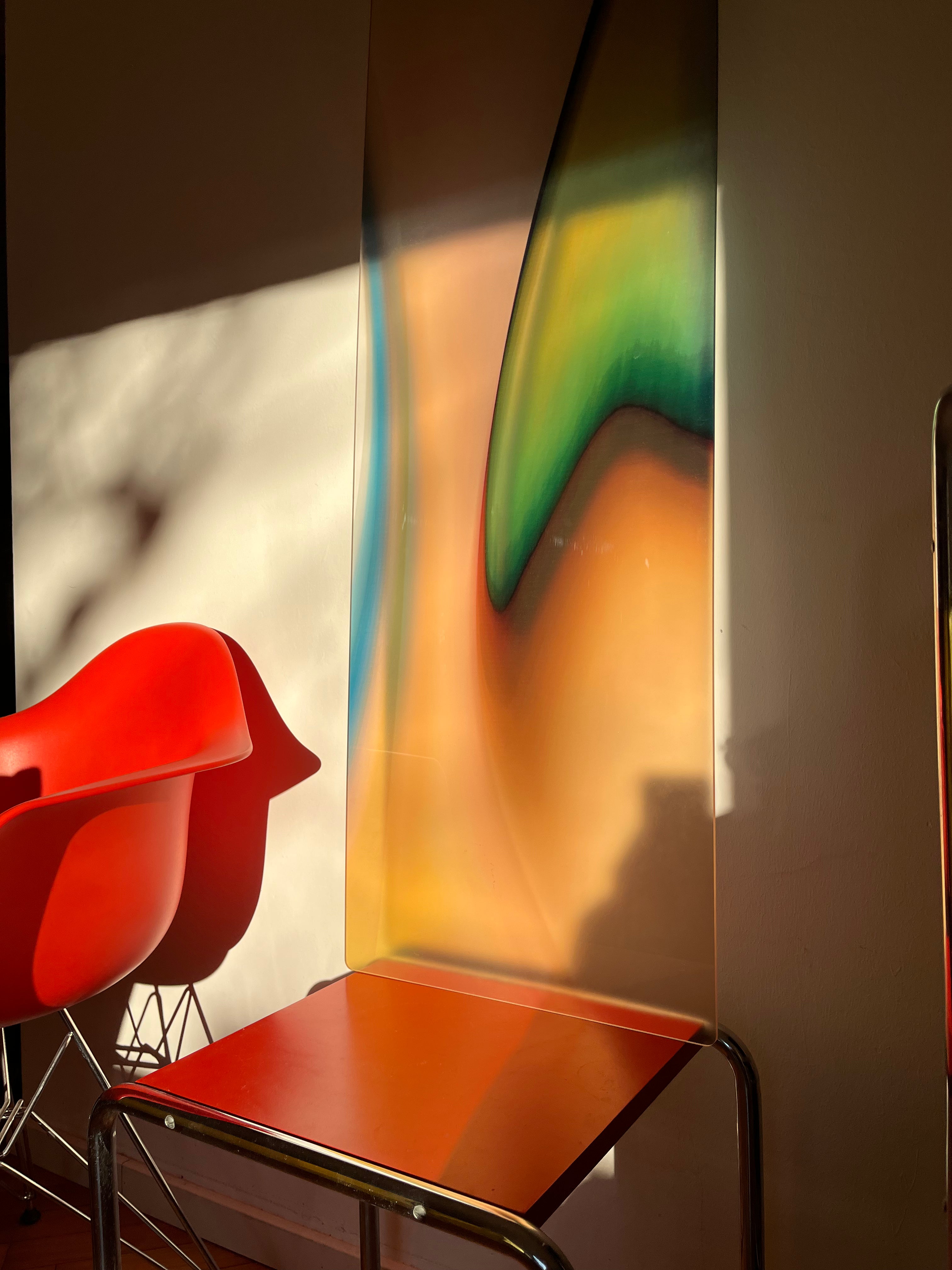 GREEN FLAME by Luis West in low sunlight, resting on a chair next to a red shell chair